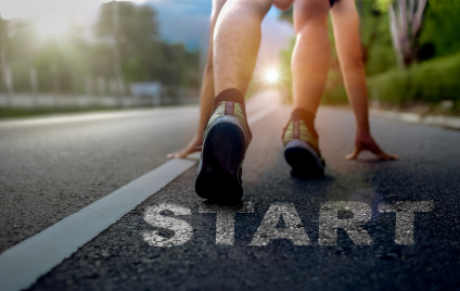 Ein Läufer in Startposition auf einer Straße im Freien bei starker Sonneneinstrahlung, der Motivation, Entschlossenheit und den Beginn einer neuen Reise symbolisiert.